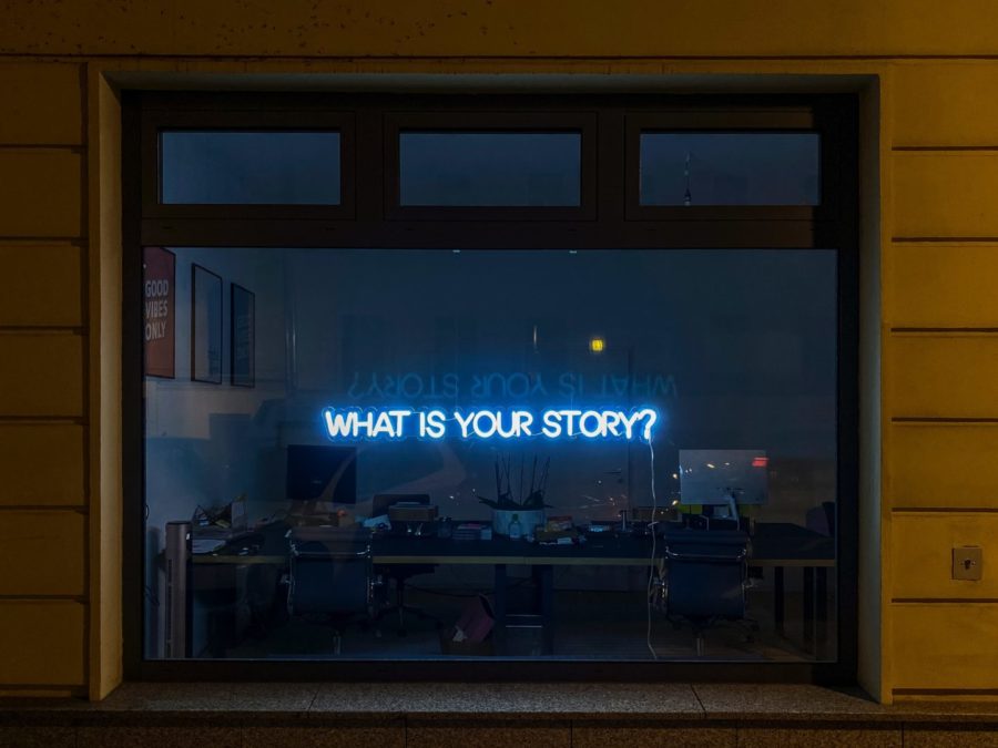 Neon sign in store-front window that reads "What's your story"